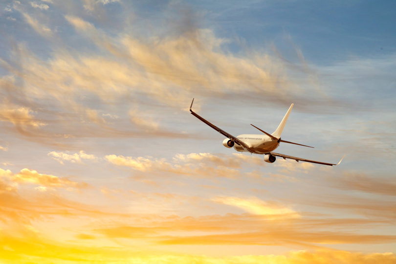 Airplane flying across a sky with golden clouds during sunset.