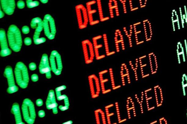Electronic departures board showing multiple scheduled times marked as “DELAYED” in red text.