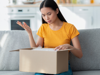 Person sitting on a sofa opening a cardboard box and looking inside a home setting.