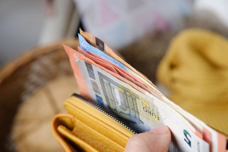 Hand holding a wallet with visible banknotes partially pulled out.